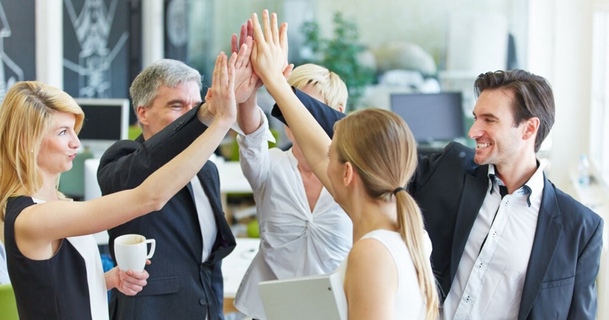 Ejecutivos y empleados de una importante empresa en un buen clima organizacional chocando manos luego de capacitarse en inglés con Wall Street English