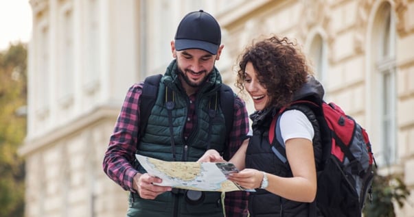 Uomo con berretto nero che dà indicazioni in inglese a una giovane donna con i riccioli