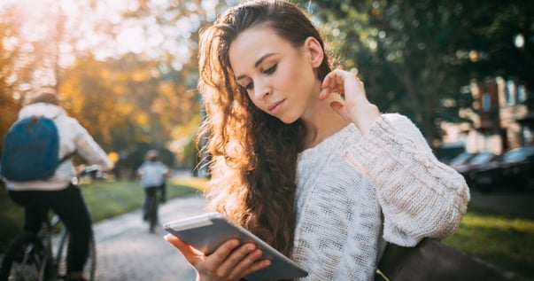 Giovane donna con riccioli seduta in un parco che guarda indicazioni in inglese sul suo tablet