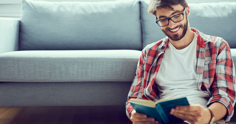 hombre con camisa y remera y anteojos negros leyendo libro en inglés en un sillón