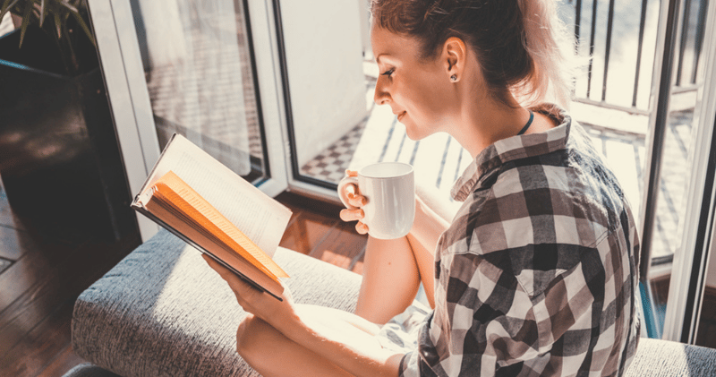 mujer con camisa y café leyendo libro en inglés en el balcón de una casa
