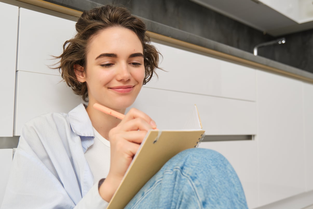 concepto-pasatiempos-estilo-vida-feliz-mujer-joven-sienta-piso-boligrafo-cuaderno-wirtes-su-di