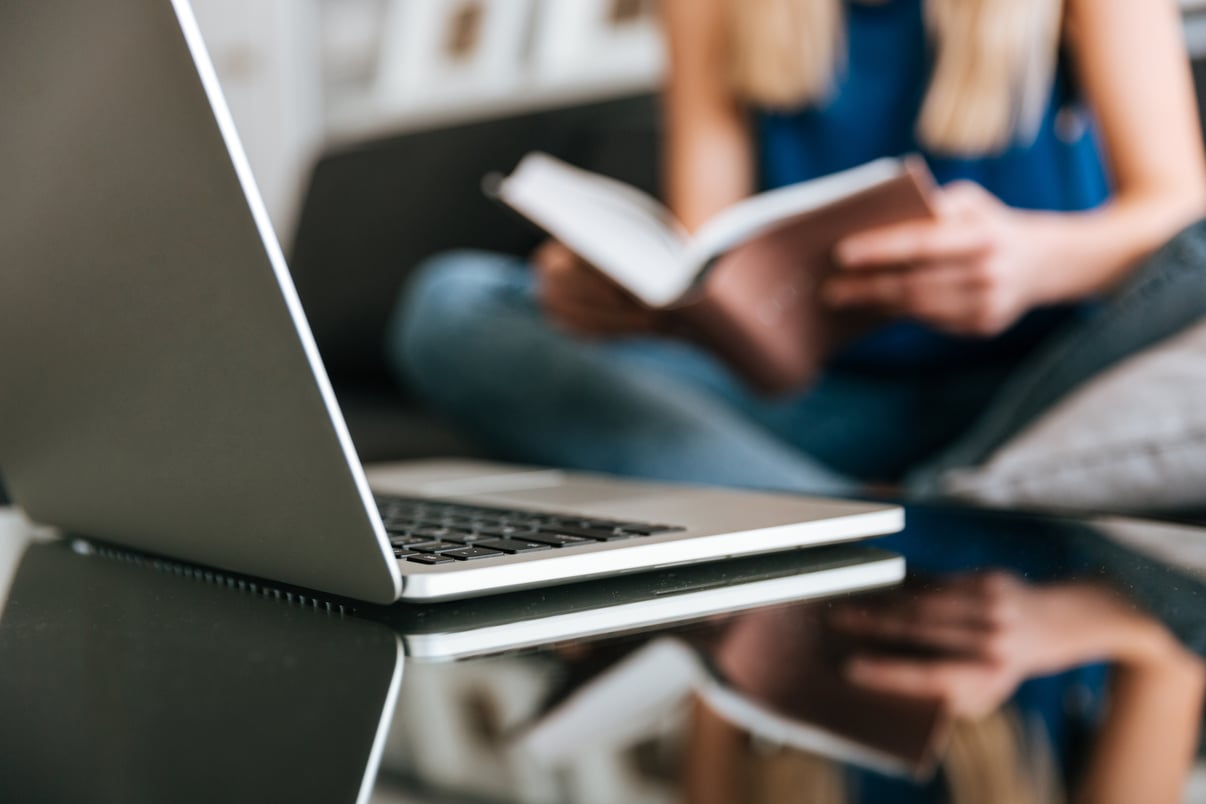 portatil-sobre-mesa-cerca-mujer-leyendo-libro-casa