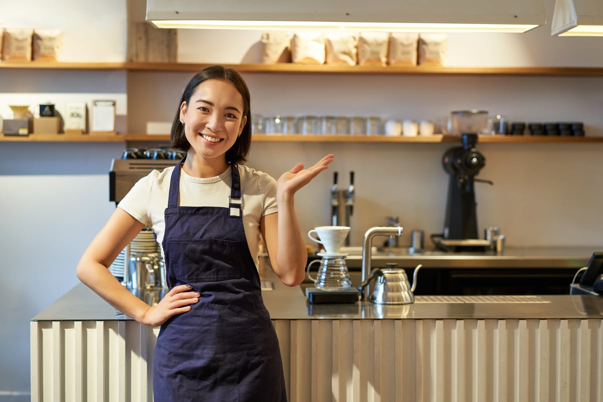 portrait-asian-girl-apron-standing-cafe-near-counter-barista-pointing-finger-copy-space