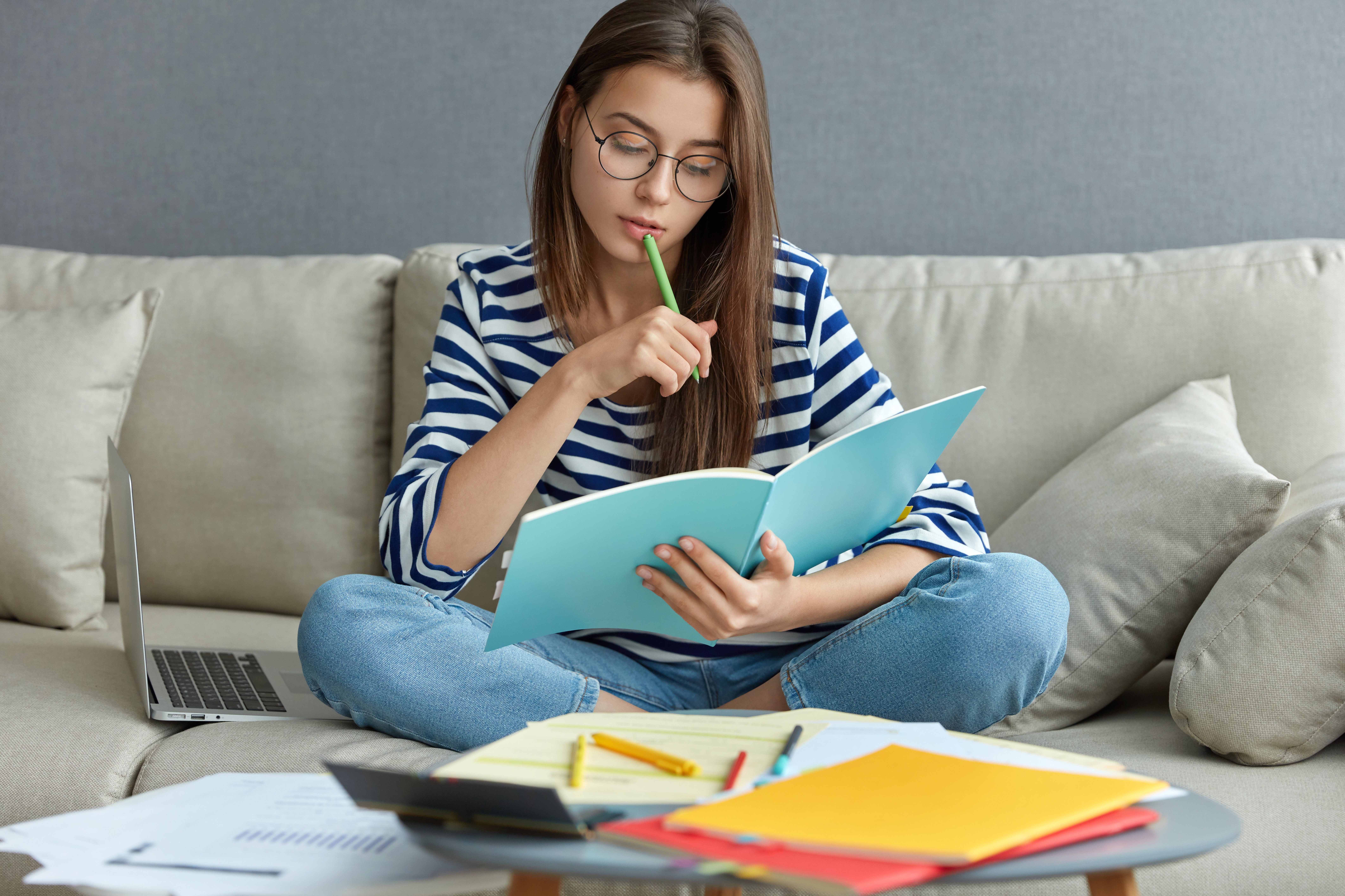 studying-online-concept-serious-young-woman-being-busy-with-remote-freelance-project-sits-at-comfortable-sofa-writes-notes-holds-textbook-use-laptop-computer-at-home-with-wireless-internet